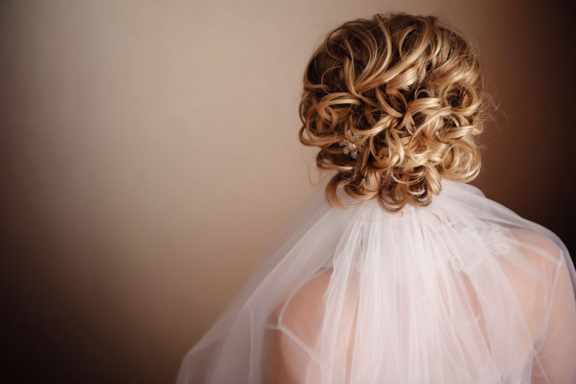 A beautiful bridal hairstyle featuring an elegant curly blonde updo accented with a white veil.