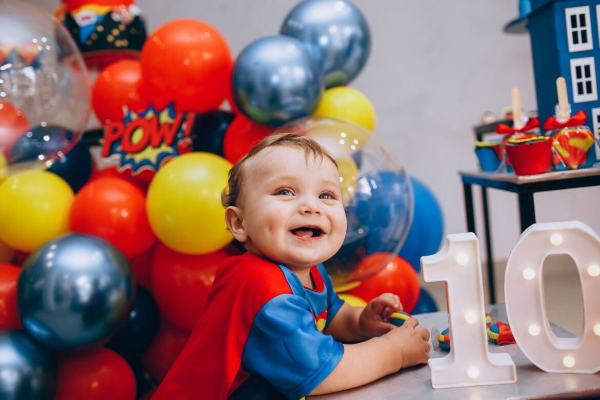 A smiling child at a colorful superhero themed birthday celebration with balloons and decorations.