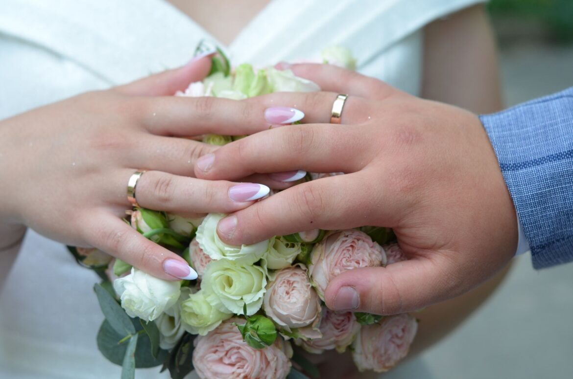 Close-up of newlyweds' hands over a bouquet of roses, symbolizing love and unity.