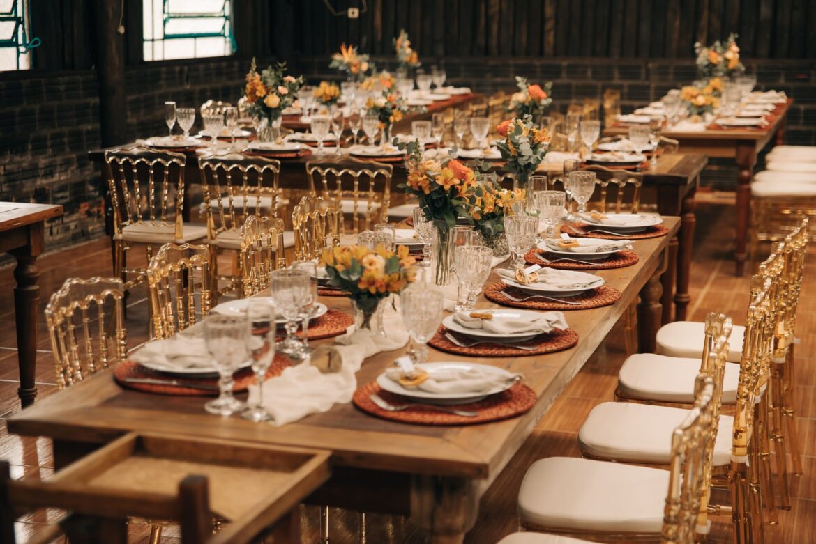 Chic wedding banquet setup with flowers, plates, and crystal glasses on long wooden tables.