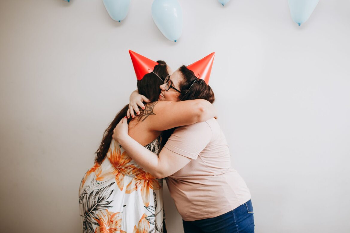 Two women hugging at a birthday party with balloons and hats, capturing joy and togetherness.