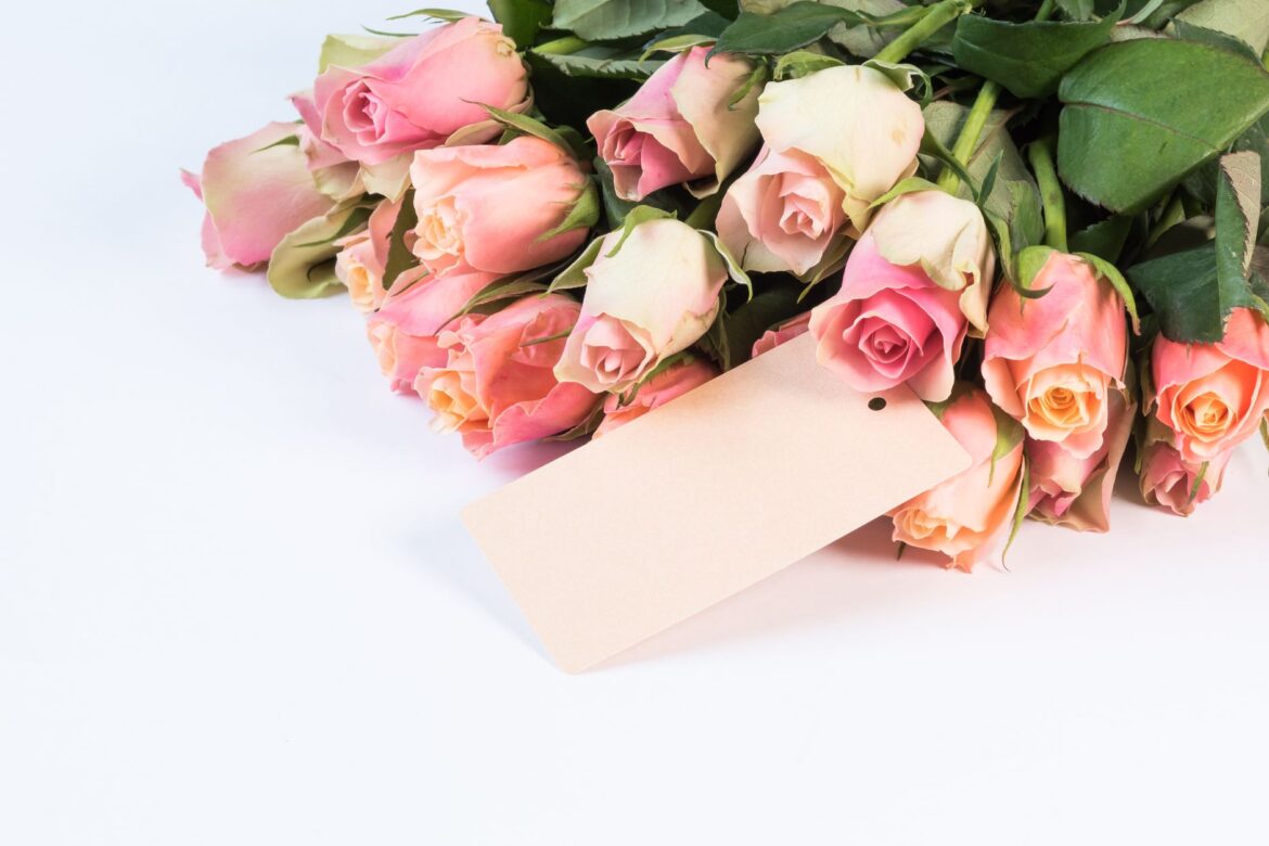 Beautiful pink roses with a blank gift tag on a white background, perfect for romantic or gift occasions.