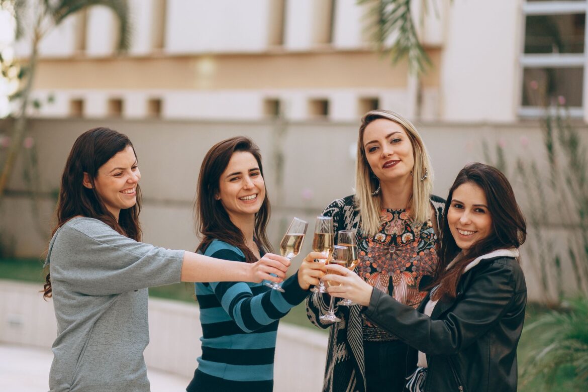 Four women smiling and enjoying a wine toast outdoors, symbolizing friendship and togetherness.