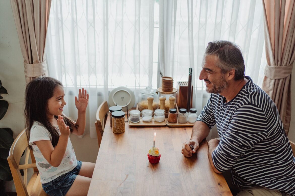 Father and daughter celebrating with a cupcake on a joyful day indoors.