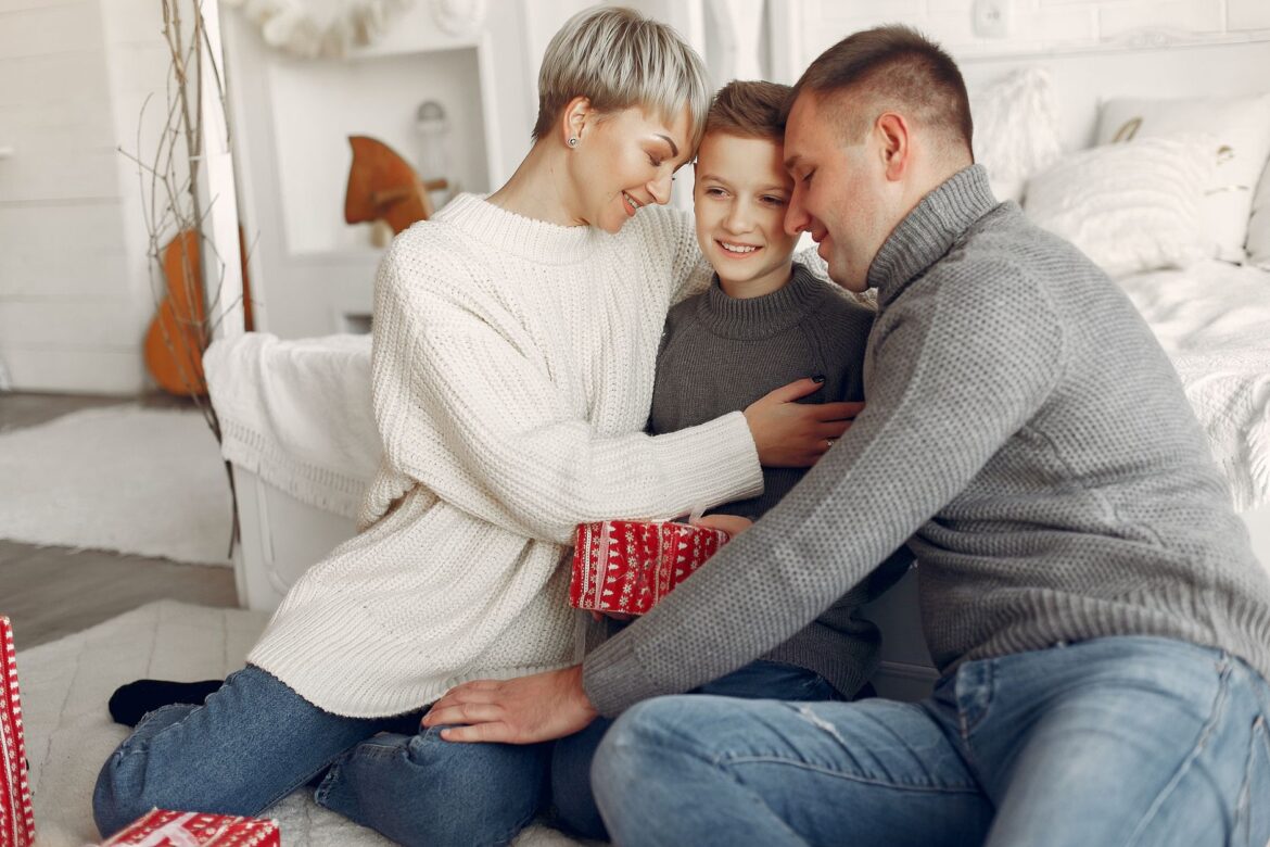 A joyful family of three sharing a tender moment while exchanging Christmas gifts indoors.