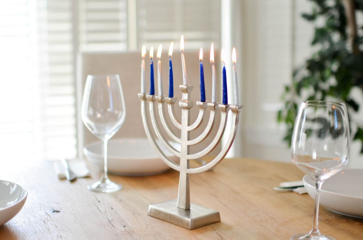A beautifully set table for Hanukkah with a lit menorah and elegant tableware.