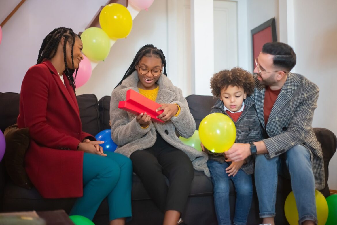 Happy family enjoying a birthday celebration with balloons, gifts, and smiles on a cozy sofa.