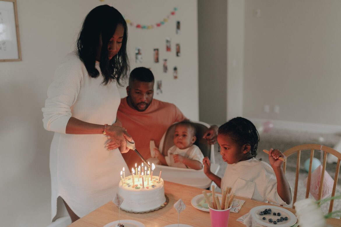 A family gathered around a table as a cake is being cut during a birthday celebration.