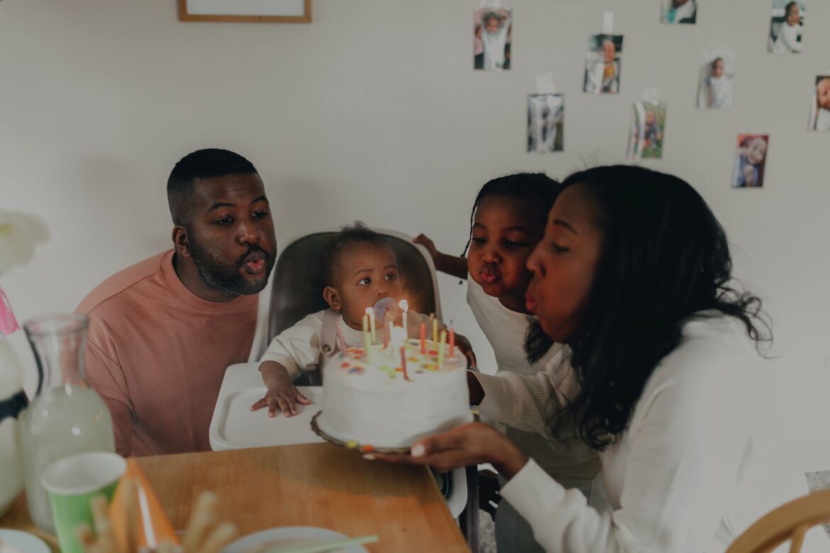 A joyful family celebrating a baby's first birthday with cake and candles indoors.