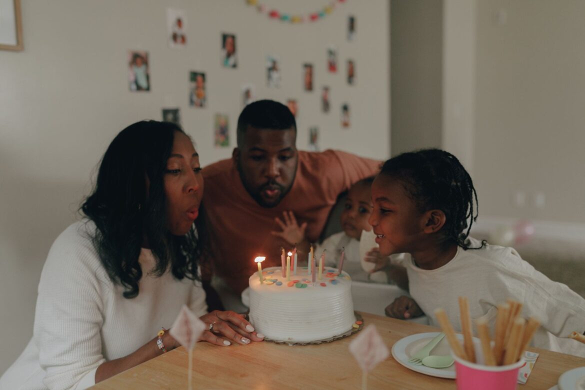 A joyful family moment as parents and children blow out birthday candles on a cake indoors.