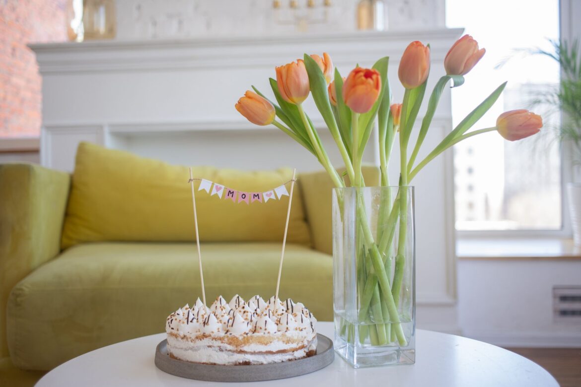 Beautiful cake with tulips in a glass vase on a table, perfect for celebrations in a cozy indoor setting.