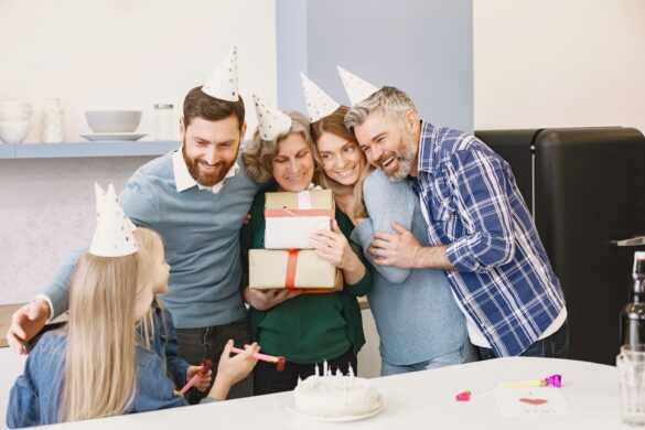 Happy family gathered indoors celebrating with gifts, cake, and party hats.