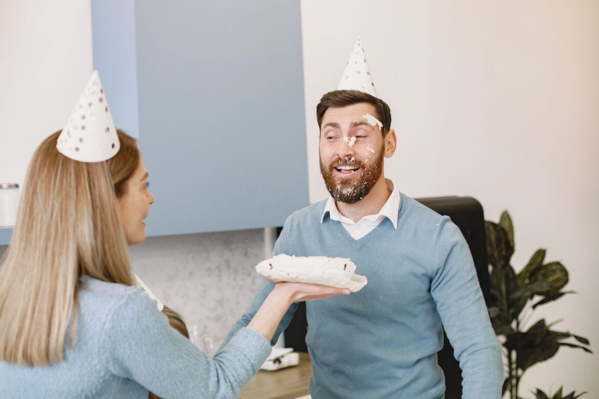 Man and woman sharing a playful cake smash during a birthday celebration indoors.