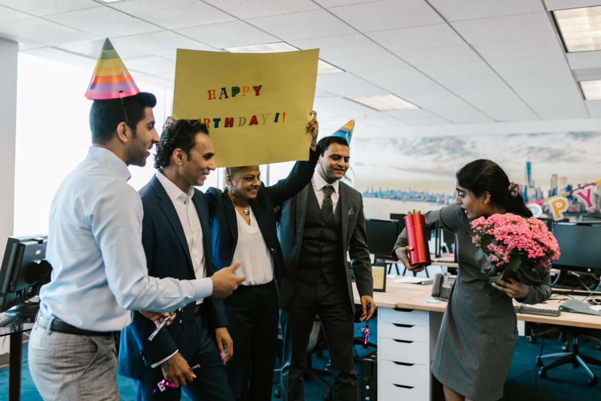 Colleagues surprise a coworker with a birthday celebration in a modern office setting.