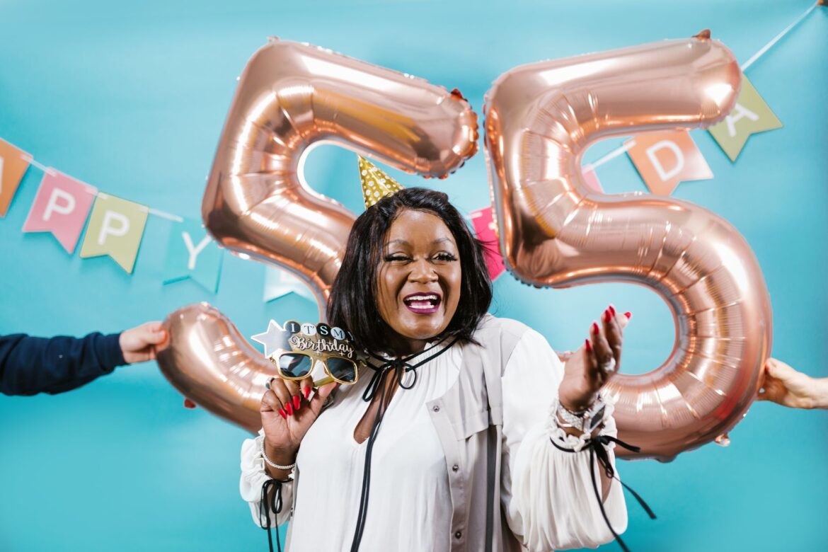 Smiling woman celebrates 55th birthday with balloons and festive decor.