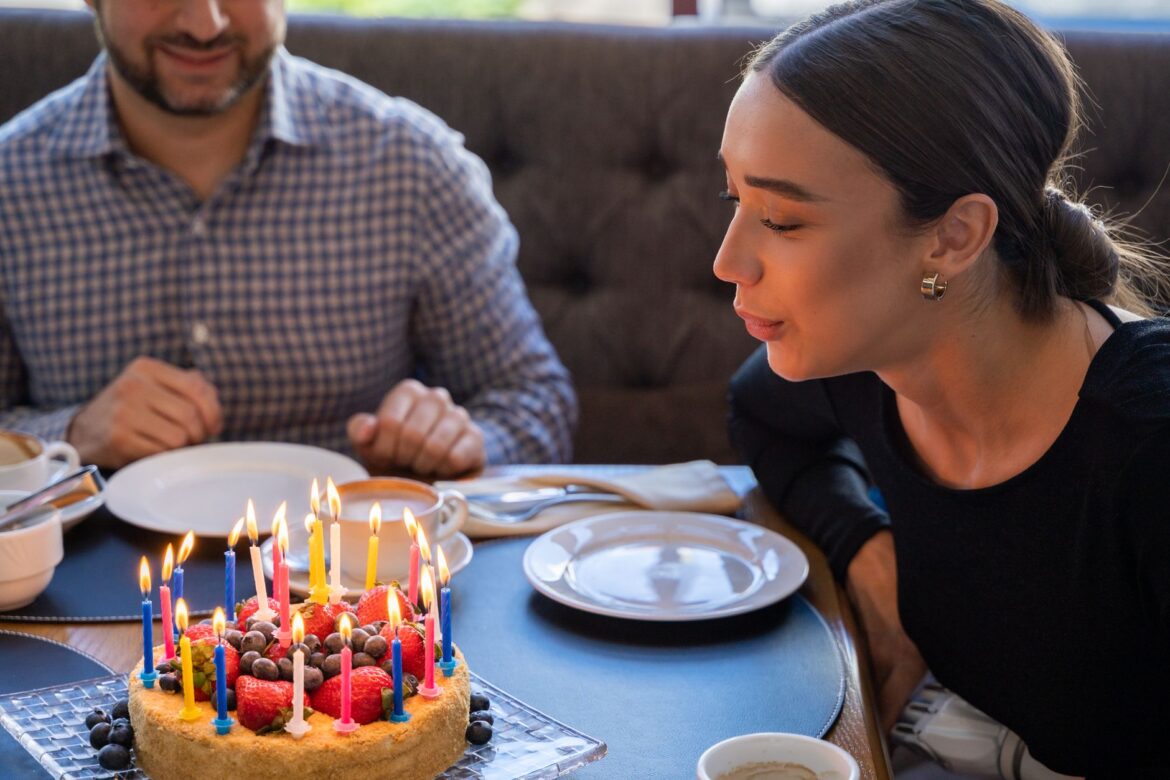 A woman joyfully blowing out candles on a fruit-topped birthday cake, sharing a festive moment.