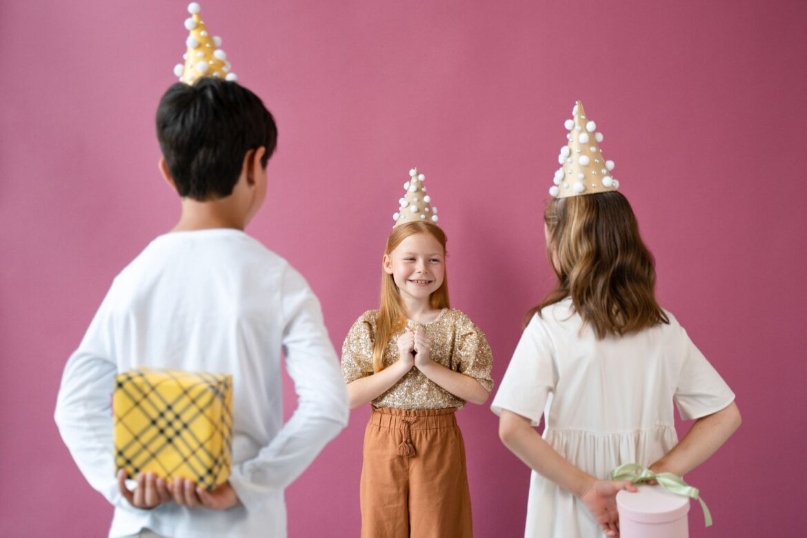 Joyful children celebrating a birthday with hats and gifts in a lively indoor setting.