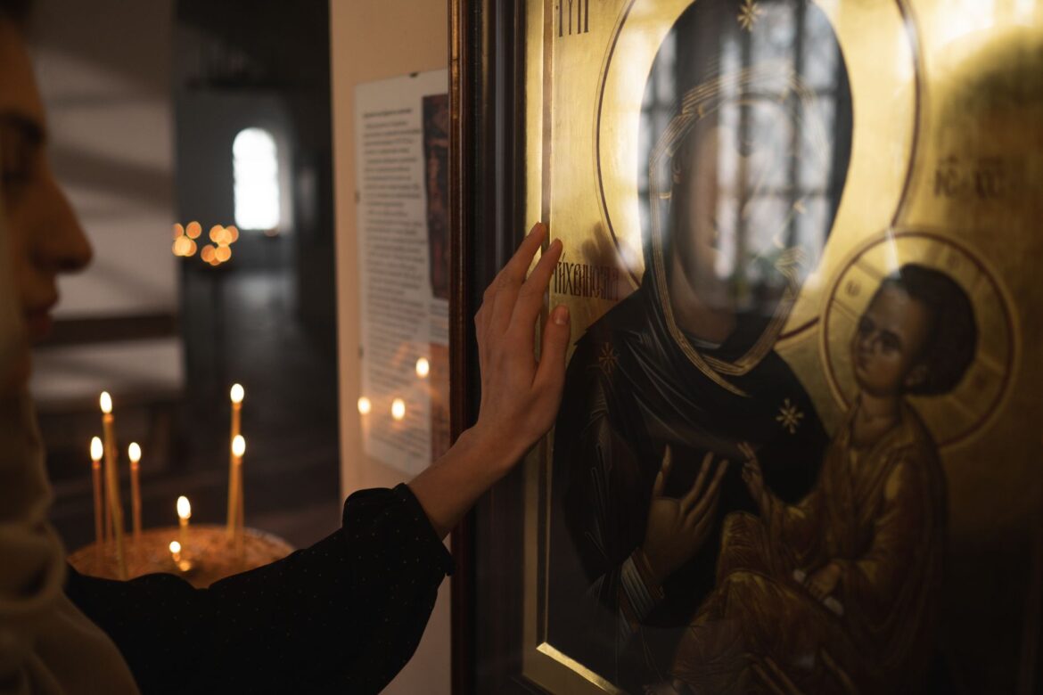 Devotional hand touching religious icon in dimly lit church interior.