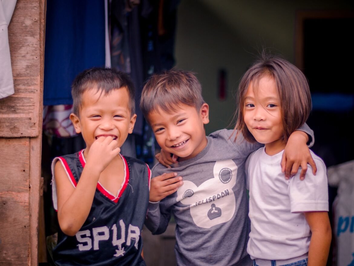 Three smiling children enjoy a happy moment together outside, showcasing friendship and joy.