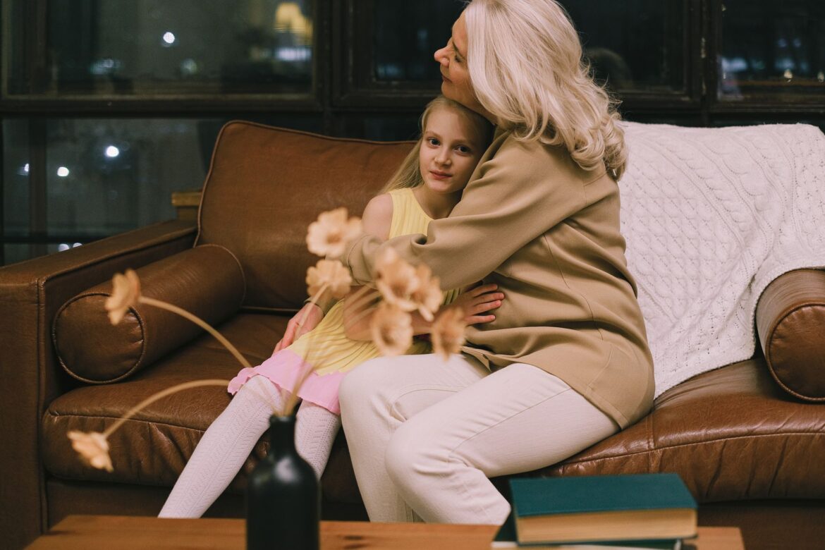Grandmother and granddaughter hugging on a sofa, sharing a warm moment indoors.