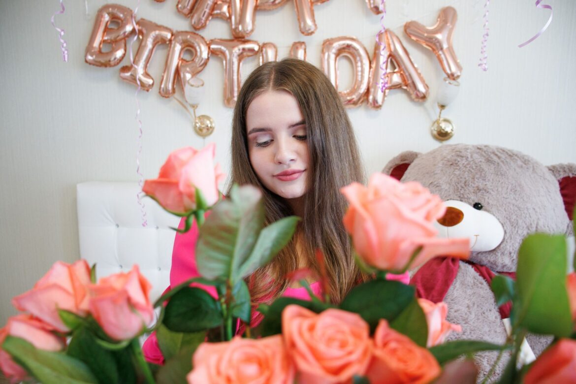A young woman celebrates her birthday surrounded by roses and festive balloon decorations.