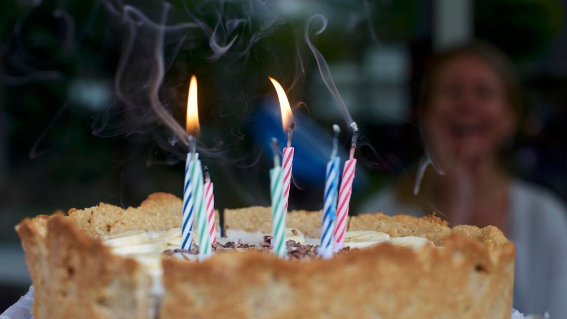Close-up of a birthday cake with lit candles and smoke, celebrating indoors with joy.