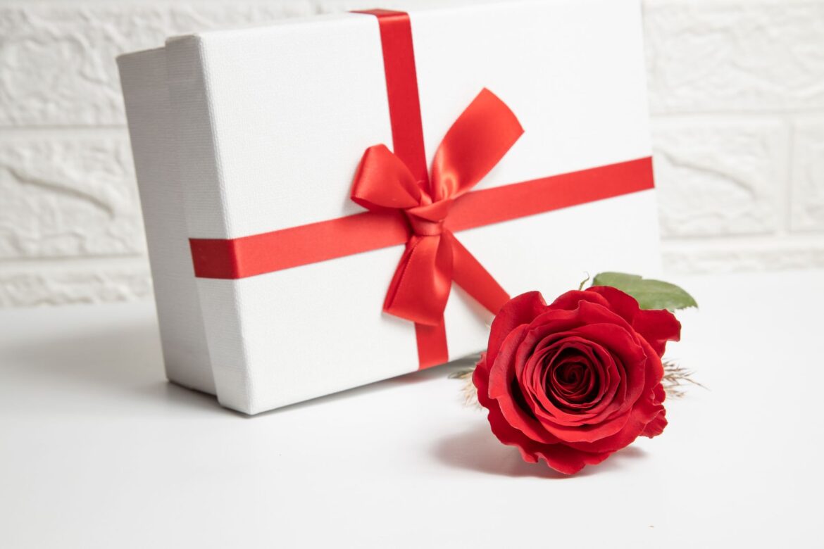 A white gift box with a red ribbon and a vibrant red rose, ideal for Valentine's Day or special romantic occasions.