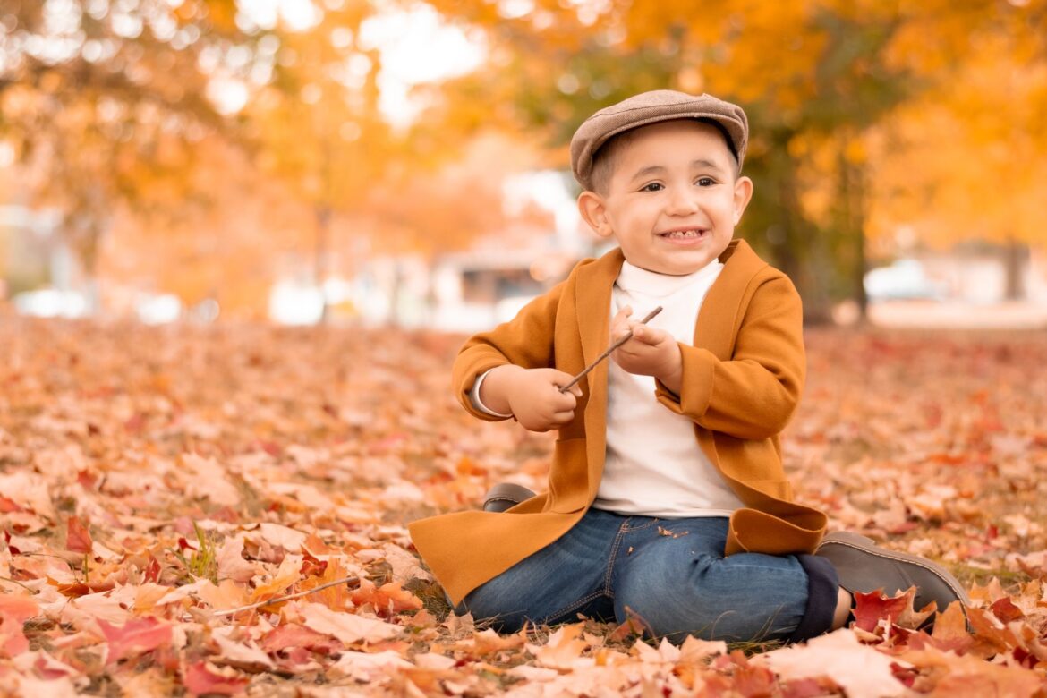 Charming autumn portrait of a child smiling amid colorful leaves.