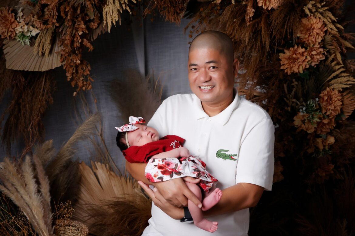 A joyful father lovingly holding his sleeping baby in an elegant floral studio backdrop.