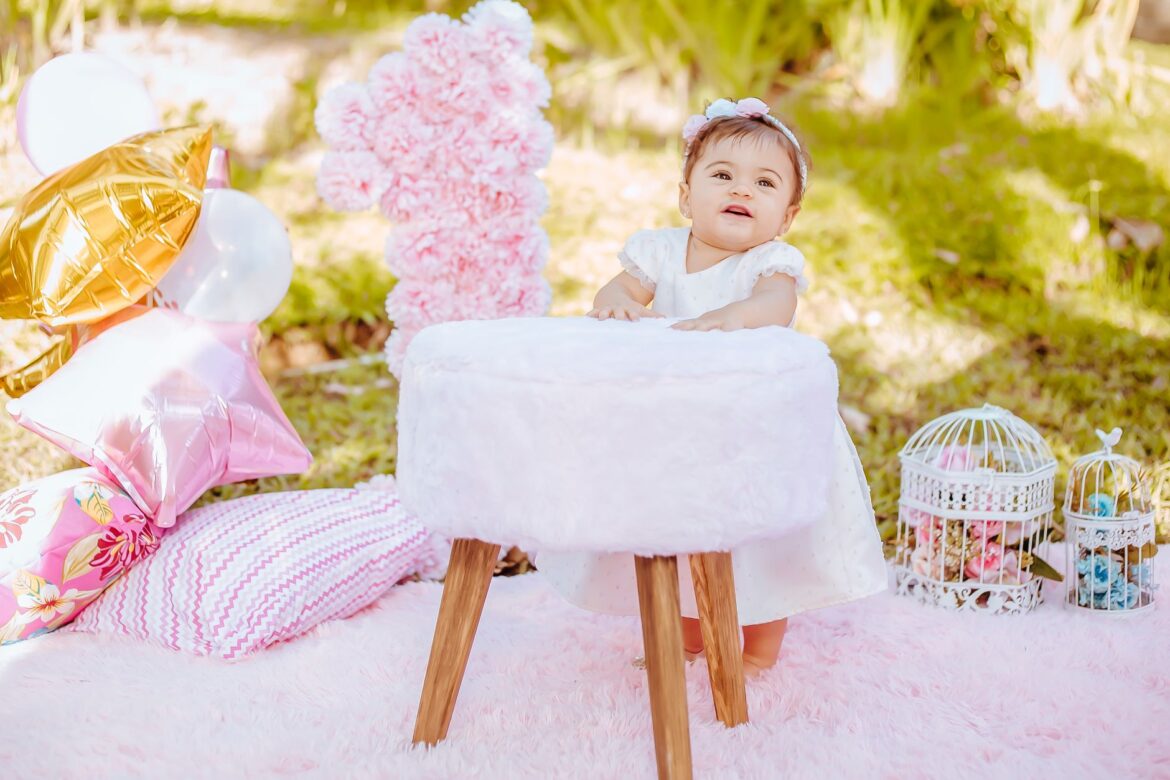 A charming outdoor birthday scene with a baby girl surrounded by decorations and balloons.