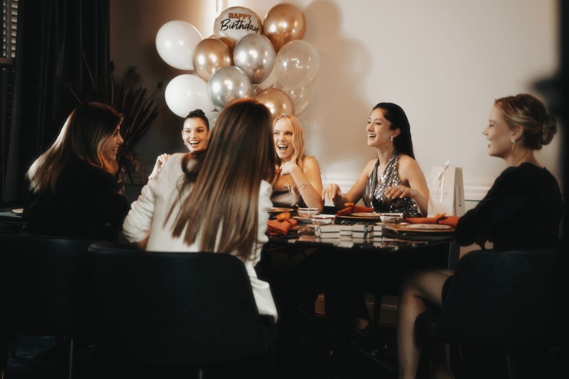 A group of joyful women celebrating a birthday with balloons indoors.