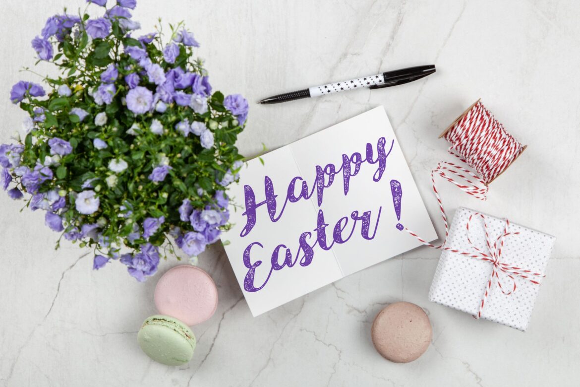 Easter greeting card with flowers, macarons, and gift on a marble surface.