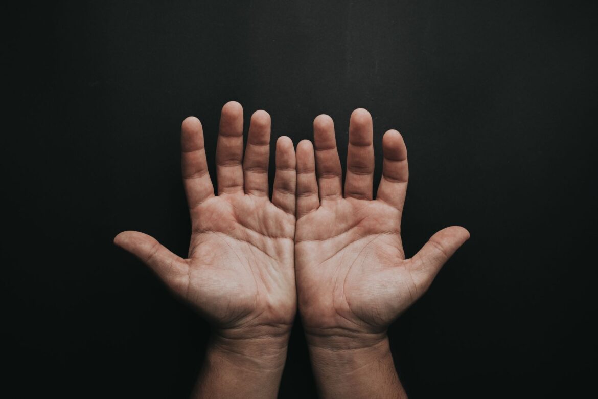 A pair of upturned hands displayed against a dark background, showcasing skin texture.