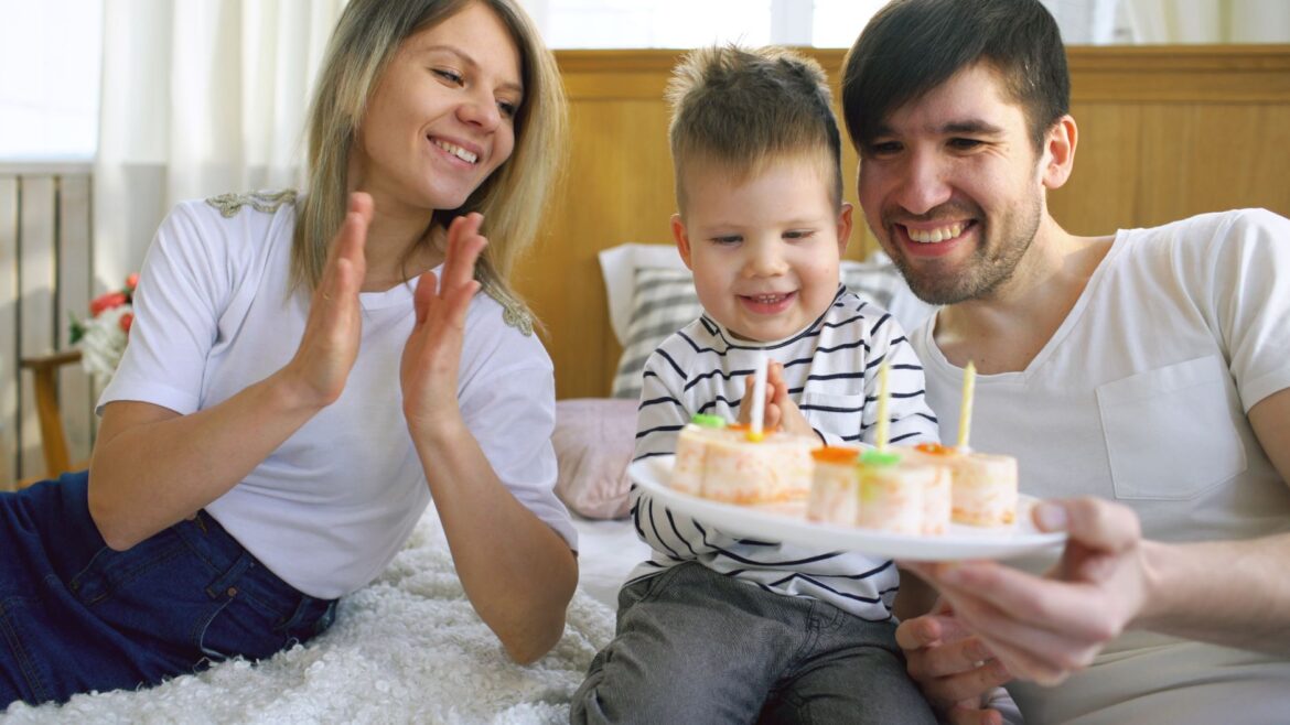 Happy family celebrating a child's birthday with cake and candles indoors.