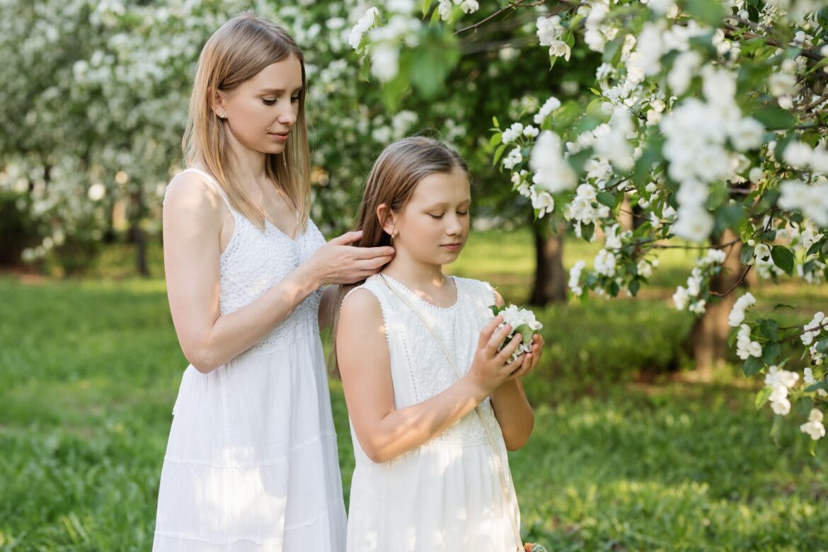 A mother and daughter in white dresses enjoying a spring day in a blooming garden.