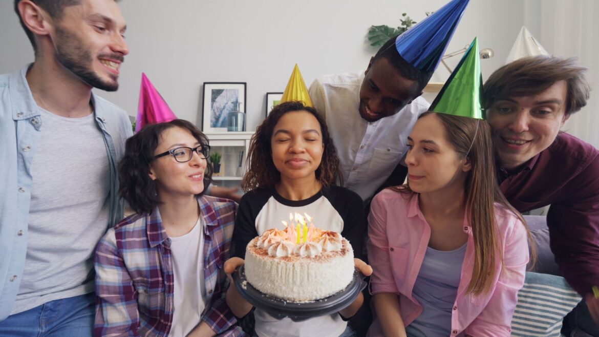Group of friends celebrating a birthday with a cake and party hats indoors.