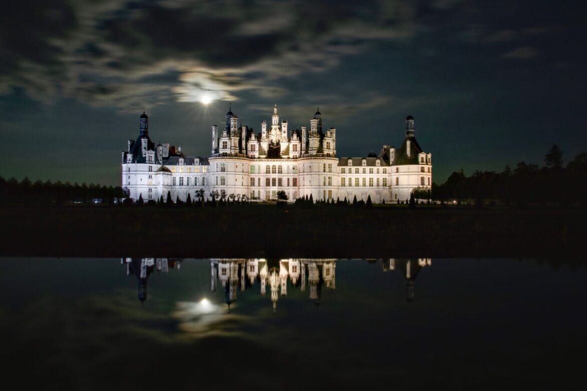 Majestic Château de Chambord illuminated under moonlight, reflecting in water.
