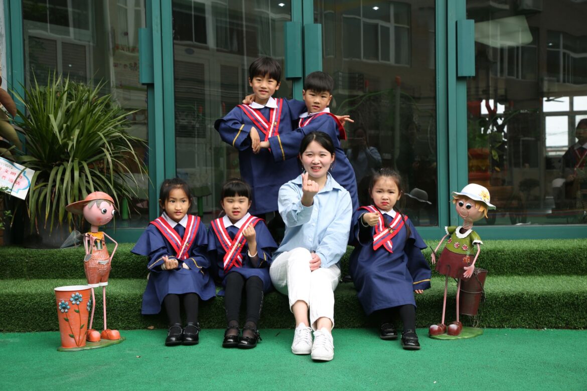 Group of children in blue graduation uniforms posing with a teacher outdoors.