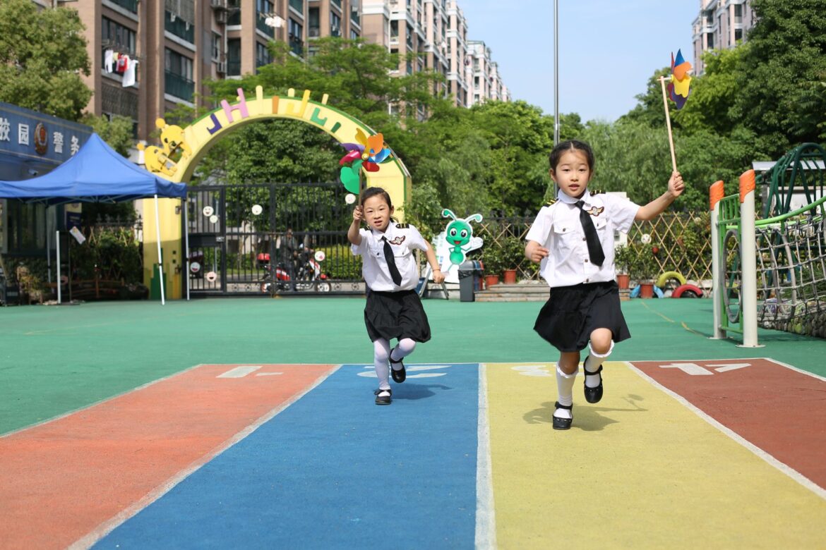 Two children happily running on a colorful track with windmills in a schoolyard
