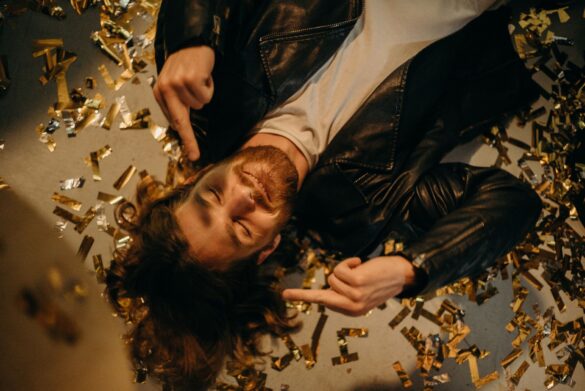 Bearded man lying on the floor, surrounded by festive confetti, expressing carefree celebration.