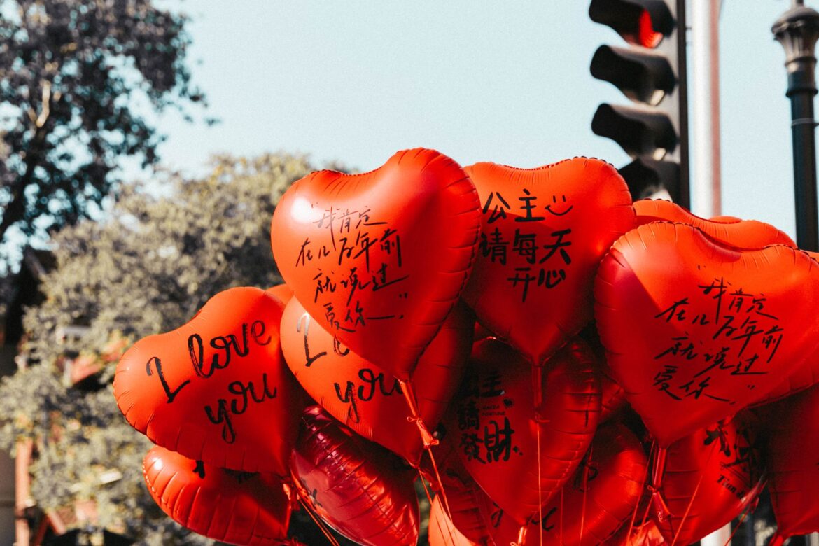 Red heart-shaped balloons with love messages in English and Chinese at an outdoor event.