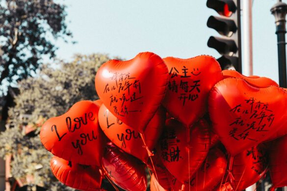 Red heart-shaped balloons with love messages in English and Chinese at an outdoor event.