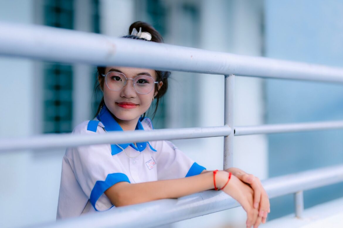 Young teen girl smiling through railing, wearing glasses and a uniform.