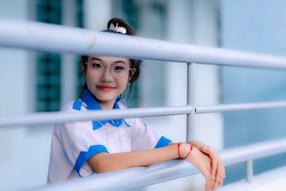 Young teen girl smiling through railing, wearing glasses and a uniform.