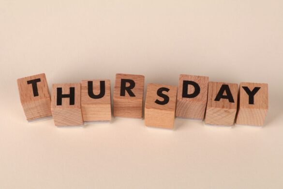 Wooden blocks arranged to spell Thursday on a neutral background.
