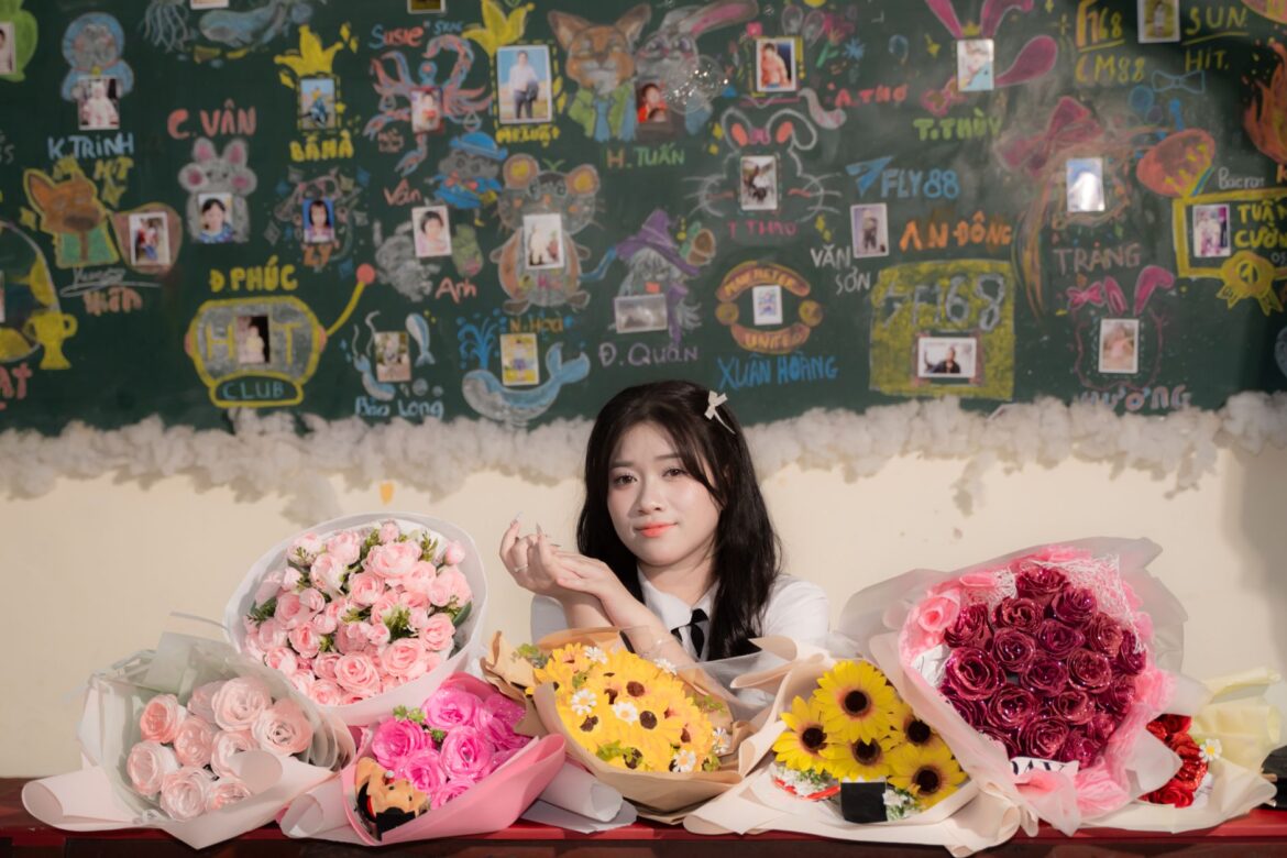 A woman sits in a decorated classroom with diverse floral bouquets on the desk.