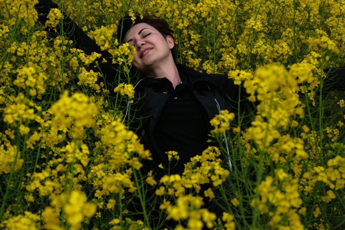 Smiling woman lying among bright yellow flowers, enjoying nature's beauty.