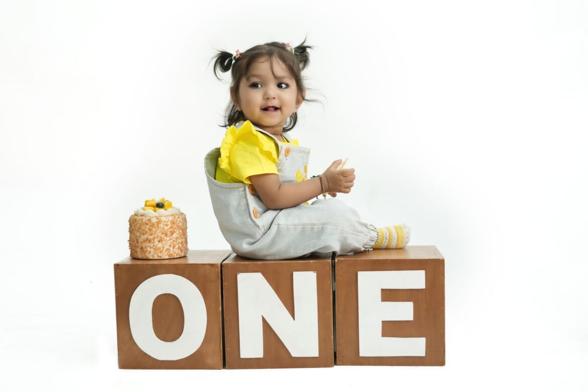 Cute baby celebrating first birthday sitting on blocks with cake and balloons.