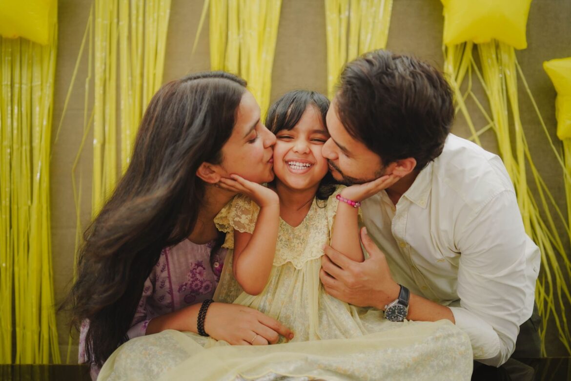 A heartwarming family moment with parents kissing their daughter during a festive celebration.