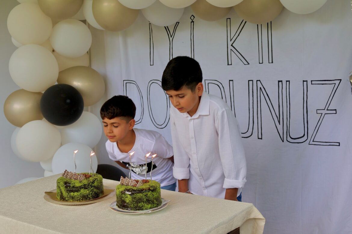 Two boys joyfully blow out candles on cakes at a birthday celebration with balloons.
